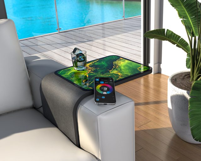 Sofa-arm table with green decorative glass, a drink and a nearby color controller beside a pool.